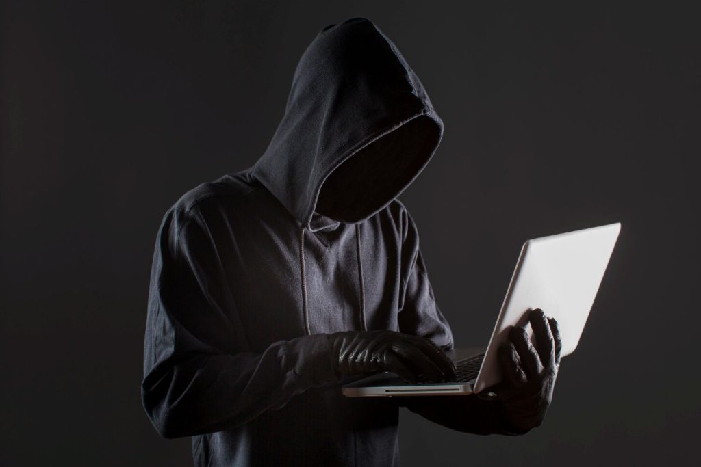 A hacker typing on a laptop with lines of malicious code on the screen, targeting a website.